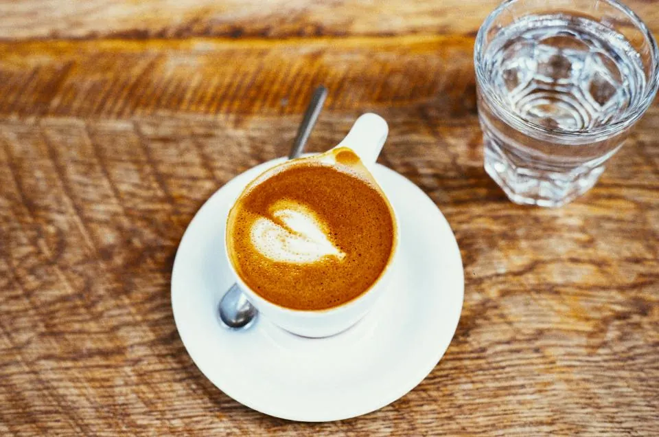 Taza de café junto a un vaso de agua sobre una mesa de madera