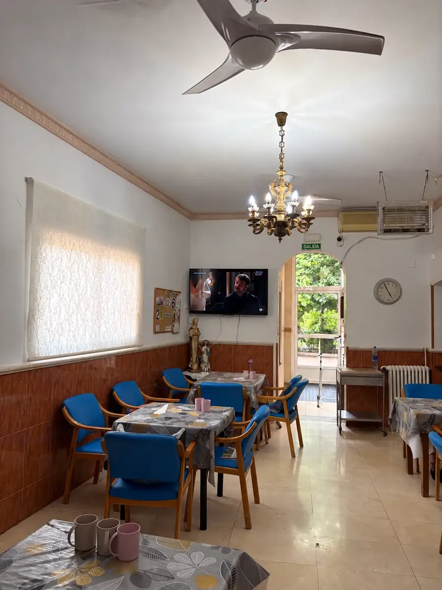 Comedor con mesas, televisión, lámpara de araña y puerta abierta al jardín