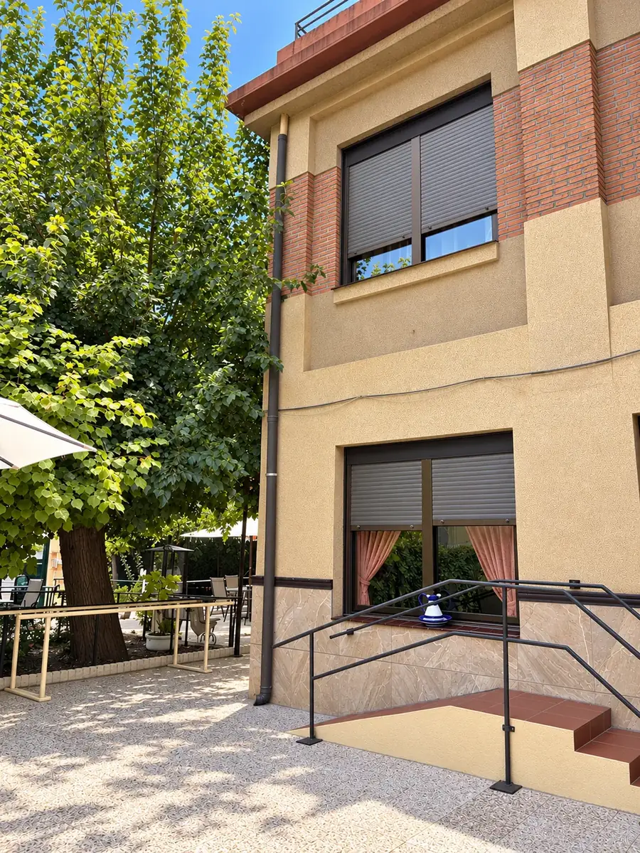 Fachada trasera con rampa de acceso, barandilla y un gran árbol junto a la terraza