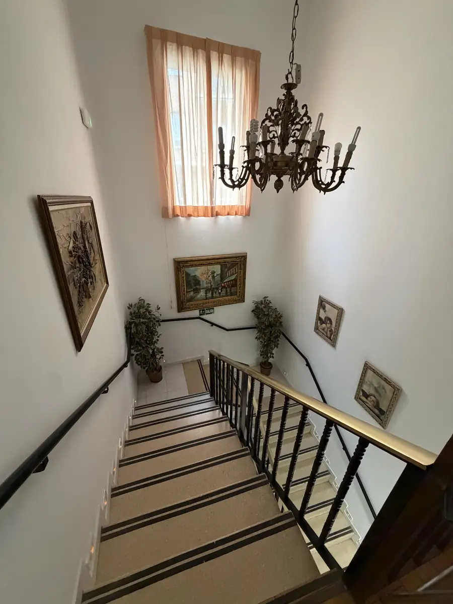 Escalera con pasamanos, cuadros y lámpara de araña