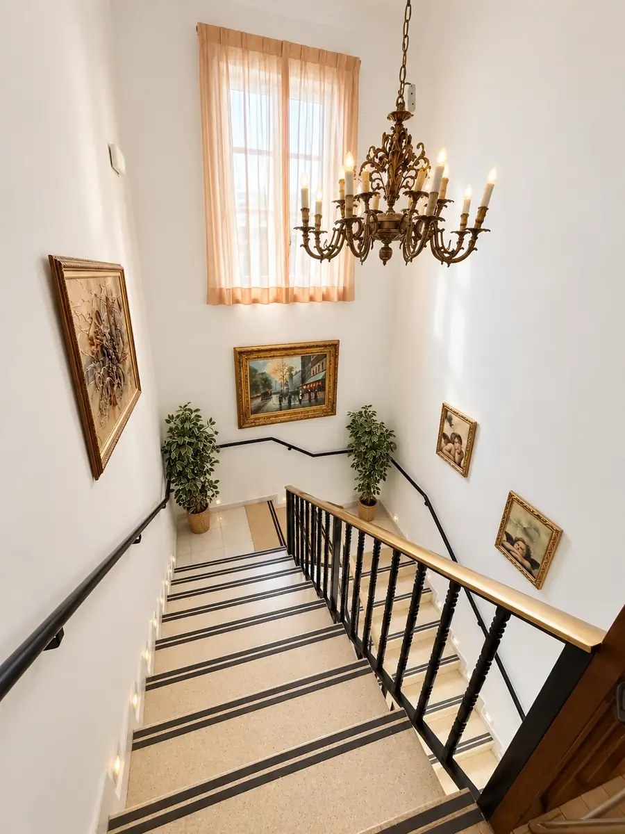 Escalera luminosa con barandilla, pasamanos, cuadros y lámpara de araña