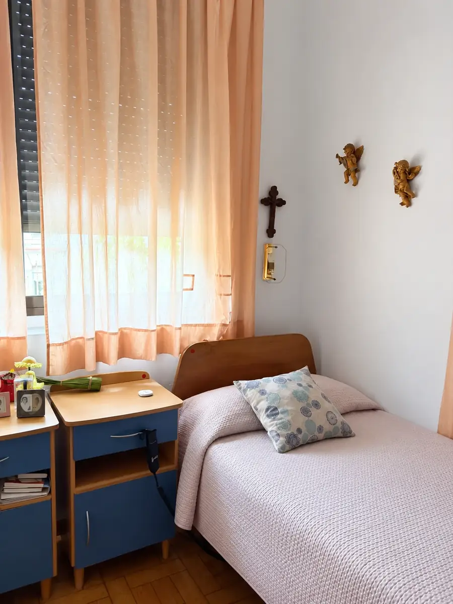 Cama con cojín de flores, mesillas con fotos y angelitos en la pared
