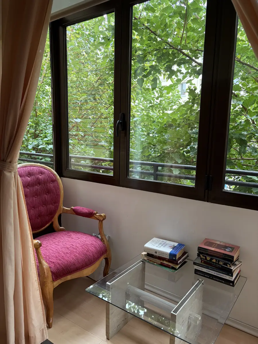 Butaca y mesa con libros junto a una ventana con vistas a los árboles