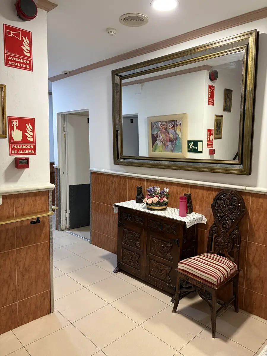 Pasillo con un gran espejo dorado, cómoda y silla antigua