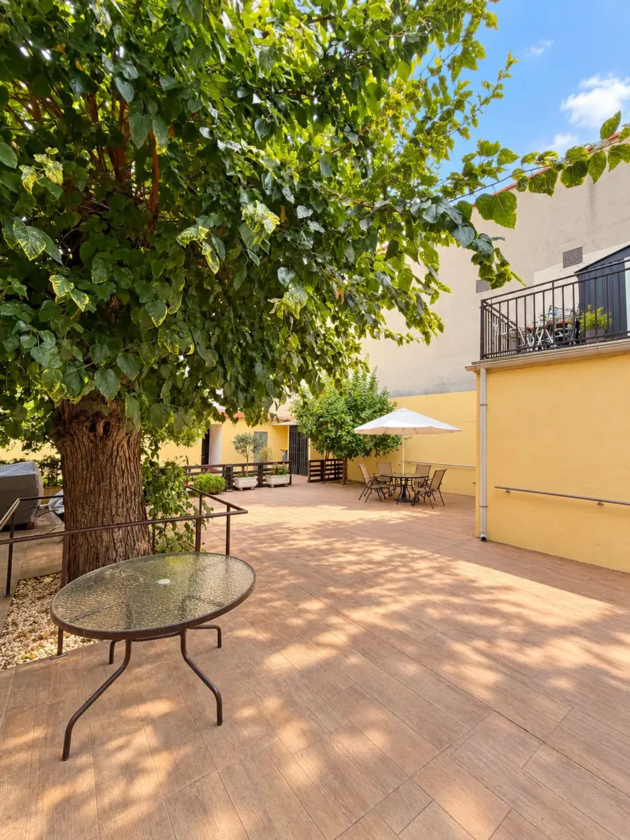 Patio soleado a la sombra de un gran árbol, con mesa redonda