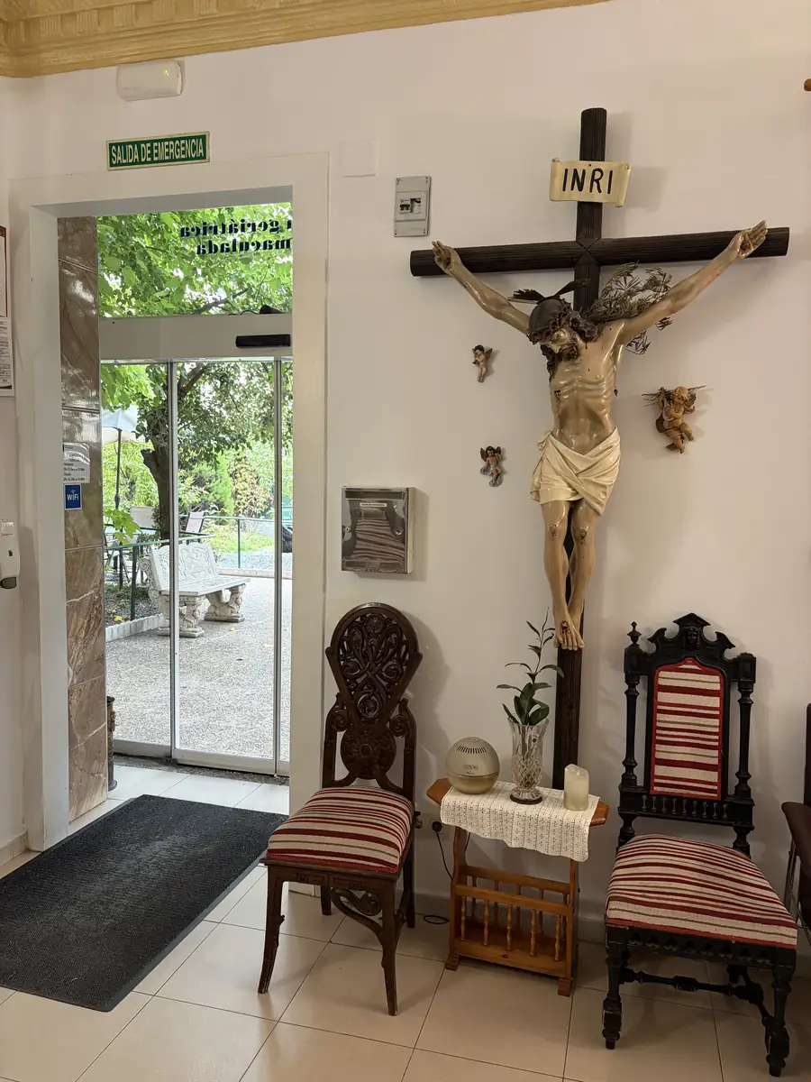 Recibidor con crucifijo, sillas antiguas y la puerta al jardín