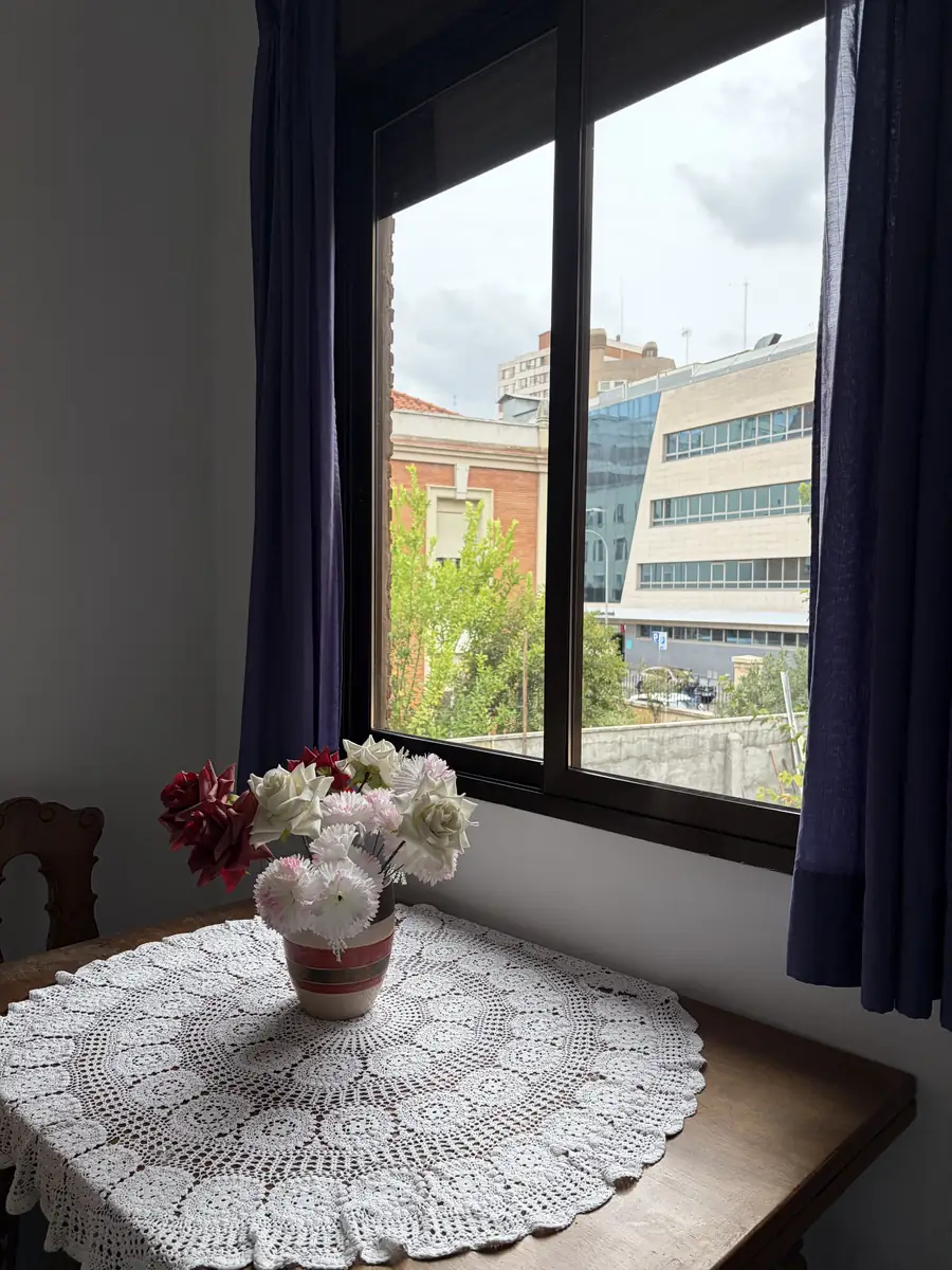 Mesa con mantel de ganchillo y flores junto a una ventana luminosa