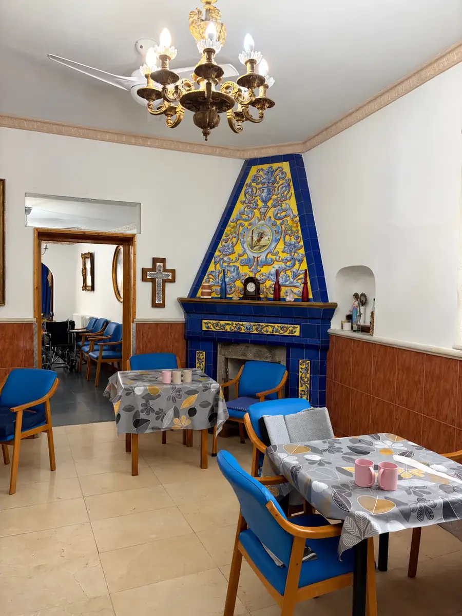 Sala común con chimenea de azulejos azules y amarillos, lámpara de araña y mesas
